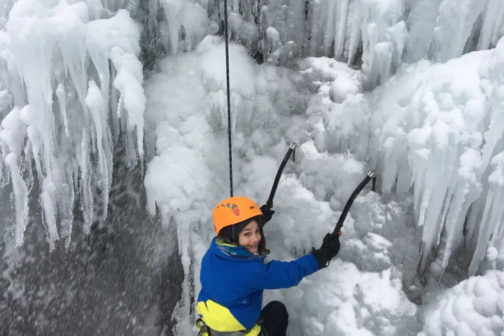 Ice climber using ice picks to climb up cliff