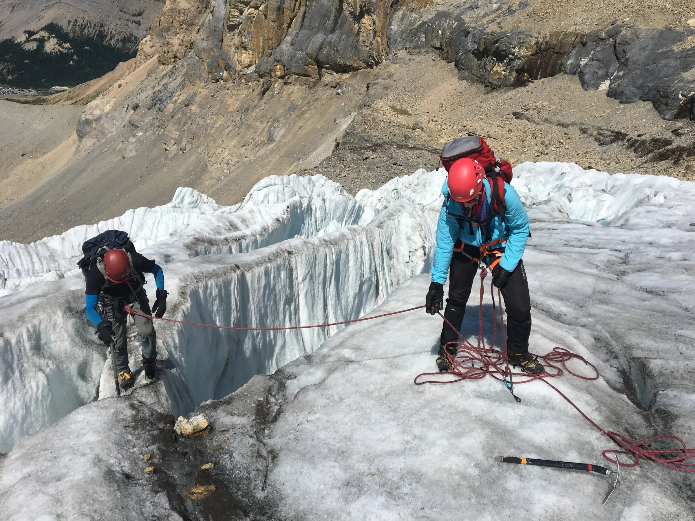 Two alpinists helping each other climb down a cravass