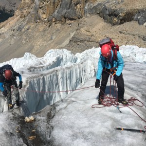 Two alpinists helping each other climb down a cravass