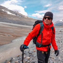 Man in red jacket looking toward camera standing in glacial valley