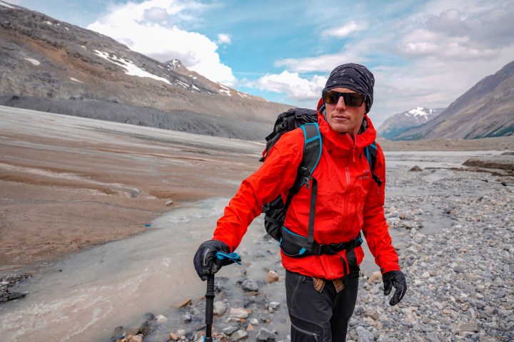 Man in red jacket looking toward camera standing in glacial valley